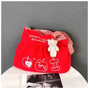 Close-up of red canvas travel bag featuring ruffles, bear charm and checkered strap
