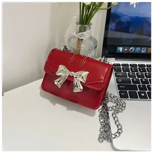 Mini red crossbody bag with silver bow detail and chain strap on a white desk