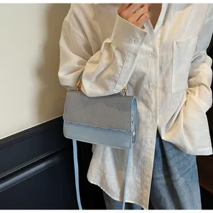 Détail du sac sous le bras bleu clair avec rabat tissé gris et finition à bords ondulés