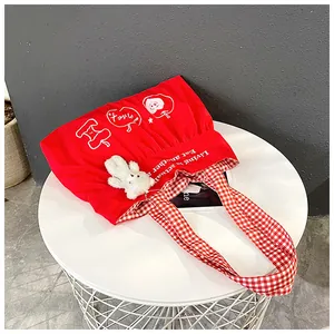 Detail of red canvas travel bag with apple print, gingham handles and bear charm