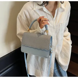 Détail du sac sous l'aisselle bleu clair avec rabat tissé et accents dorés sur modèle