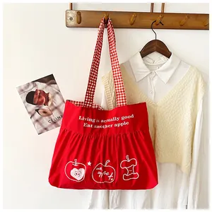 Detail of red canvas tote bag with checkered handles and a minimalist apple print