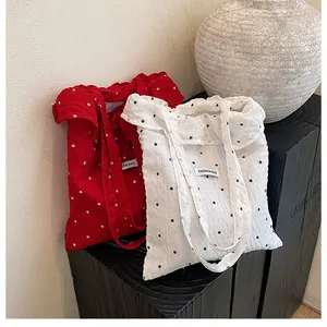 Detail of red and white pleated tote bags with floral patterns on a dark wooden base