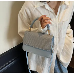 Détail du sac à bandoulière bleu clair avec rabat tissé et finitions métalliques dorées