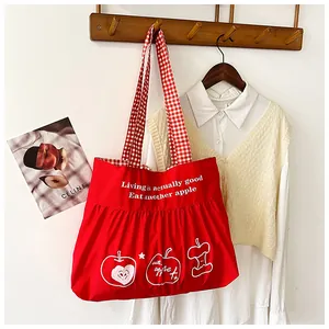 Detail of red canvas tote bag featuring apple print and red checkered straps on a hanger