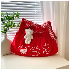Close-up of red travel tote with apple print, plaid straps and plush bear charm