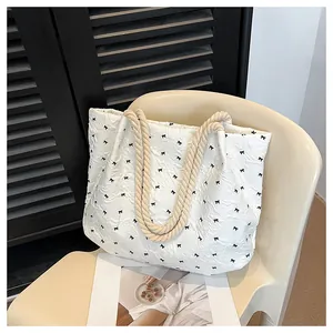 Détail du sac cabas blanc texturé à motifs nœuds et anses en corde beige sur une chaise