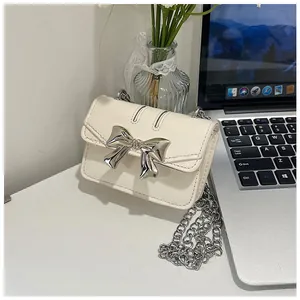 Detail of cream mini crossbody bag featuring a shiny silver bow clasp and chain strap