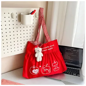 Red canvas tote bag with check handles and a cute plush bear charm on a wall hook