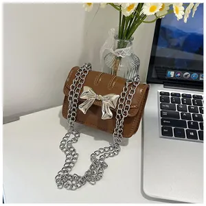 Close-up of brown mini crossbody bag featuring a large silver metallic bow buckle and chain