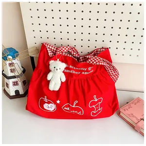 Detail of red travel tote with apple print, gingham handles and a plush bear charm