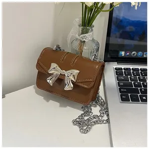 Close-up of brown leather mini crossbody bag featuring a metallic silver bow and chain
