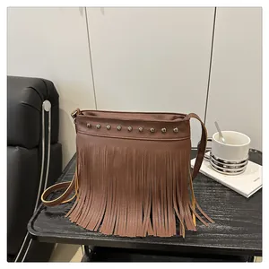Detalle de bolso bandolera bohemio marrón con flecos y remaches sobre un sofá