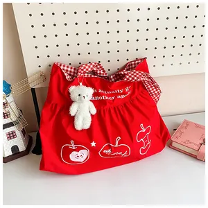 Detail of red travel bag with apple print, plaid handles, and cute plush bear charm