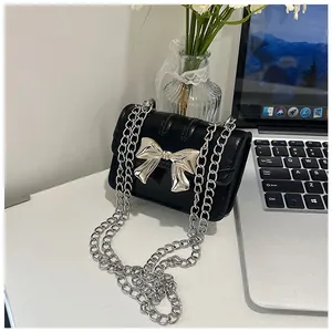 Detail shot of mini black faux leather crossbody bag with silver bow and metal chain