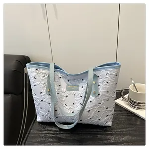 Detail view of white textured tote with black bow embroidery and blue leather handles