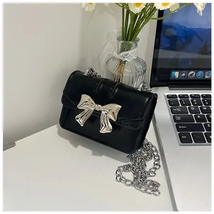 Detail of a black leather mini crossbody bag featuring a large silver metal bow accent
