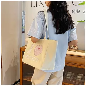 Detail of white corduroy tote bag featuring a pink plush heart and wide shoulder strap