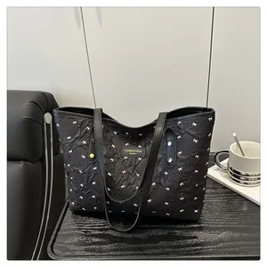 Detailed close-up of a black quilted tote bag with white bow prints and brand nameplate