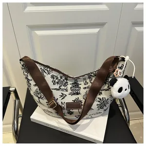 Detail of canvas half-moon bag with ink-style print, wide strap and panda plush pendant