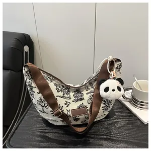Detail of hobo canvas bag with landscape print, brown woven strap and panda plush charm