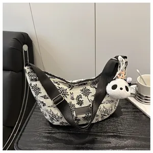 Detail of canvas crescent bag with black landscape sketch and plush panda charm