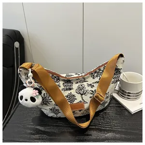 Detail of canvas crescent bag with landscape print and plush panda charm on black surface