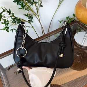 Dettaglio borsa hobo nera con catena d'argento e perla di metallo su un tavolo di vetro