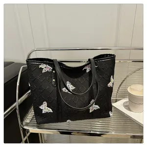 Détail du sac cabas noir avec broderies papillons colorées et texture gaufrée