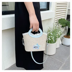 Détail du sac en paille d'été avec dentelle blanche, nœud bleu et logo de la marque