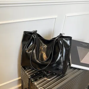 Grand sac fourre-tout noir brillant avec nœud argenté sur une valise élégante