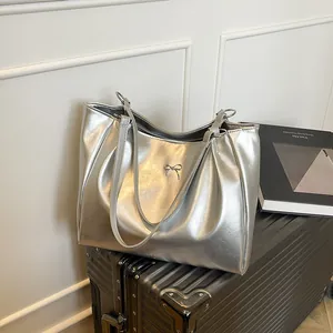 Grand sac cabas argenté avec nœud métallique posé sur une valise texturée