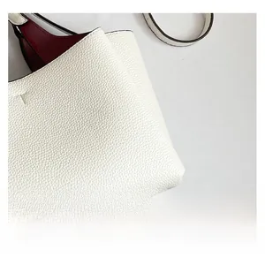 Detail of white pebble leather tote bag featuring red lining and protective metal stud