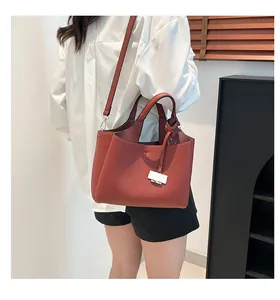 On-shoulder view of a brick red soft leather bucket bag with top handles and strap