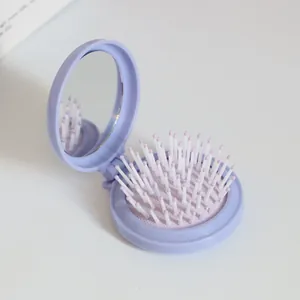 Makro-Detail der lila faltbaren Haarbürste mit Make-up-Spiegel und weichem Luftpolster