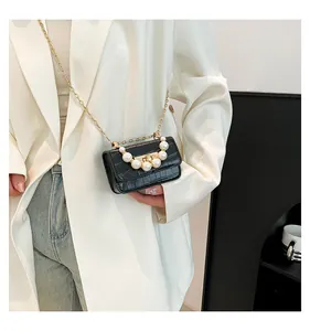 Detail of black croc-effect micro bag with pearl handle and golden chain on a white blazer