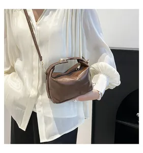 Détail du sac seau en cuir marron foncé avec poignée incurvée et fermeture éclair argentée