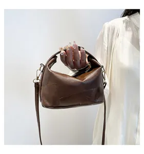 Détail d'un sac seau en cuir marron foncé avec texture brillante et boucles dorées