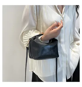 Détail du sac seau géométrique noir avec finitions dorées sur une blouse blanche