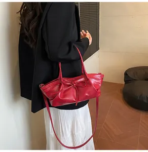 Detail of red ruched leather handbag with decorative bow knot and thin shoulder strap