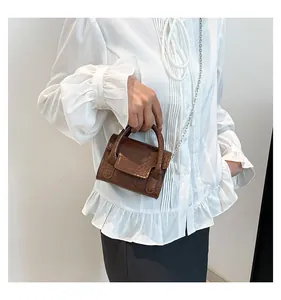 Détail d'un mini sac marron à motif crocodile avec poignée ronde et chaîne argentée