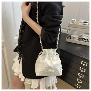 Detail of white lace drawstring bucket bag featuring 3D floral accents and pearl strap