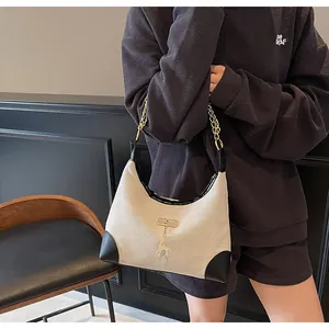 Close-up of beige canvas tote with black leather trim, gold deer charm and chain strap