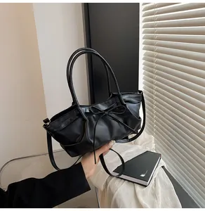 Detail of black bow handbag featuring matte leather texture and elegant pleated side design