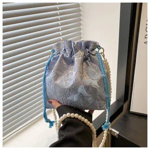 Detail view of light blue bucket bag with 3D butterfly appliques and pearl strap