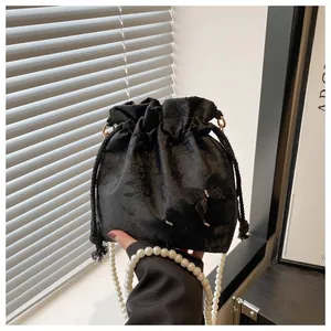 Detailed view of black bucket bag with floral jacquard pattern and elegant pearl strap