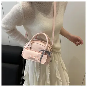 Detail of pink bow-tied crossbody bag worn by model over a soft beige knit sweater