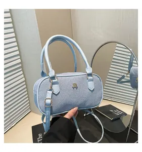 Detail of light blue cylinder bag showing woven texture and gold logo with mirror reflection