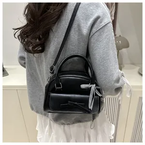 Detail of a black bow-tie handbag with ribbon charm worn as a crossbody shoulder bag