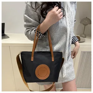 Detail of black nylon tote bag with brown leather handles worn by a casual model in studio
